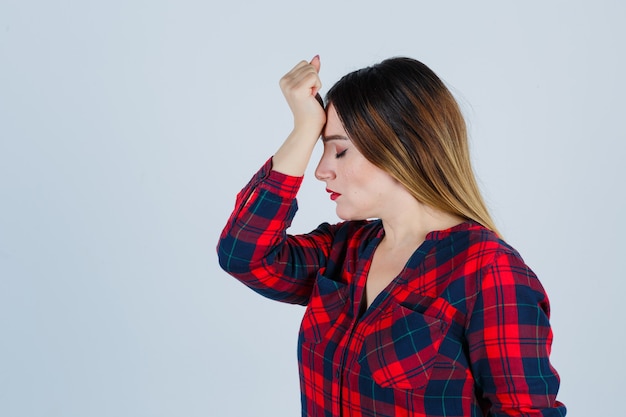 Portrait of young beautiful female with hand on forehead in casual shirt and looking pensive front view