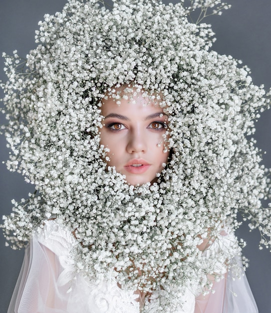 Free photo portrait of a young beautiful girl with circle made of fresh gypsophila on the face dressed in white blouse