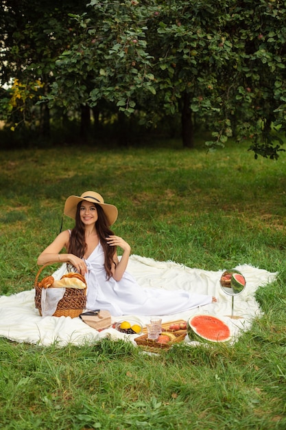 Free photo portrait of a young beautiful girl with even white teeth, a beautiful smile in a straw hat and long white dress have a picnic in the garden