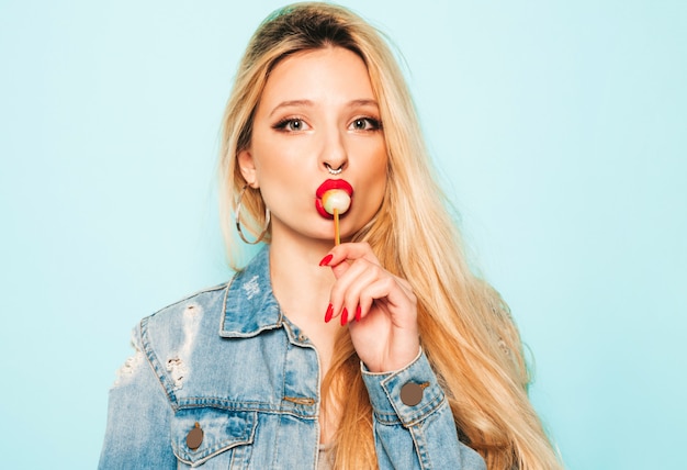 Portrait of young beautiful hipster bad girl in trendy jeans  clothes and earring in her nose.  Positive model licking round sugar candy