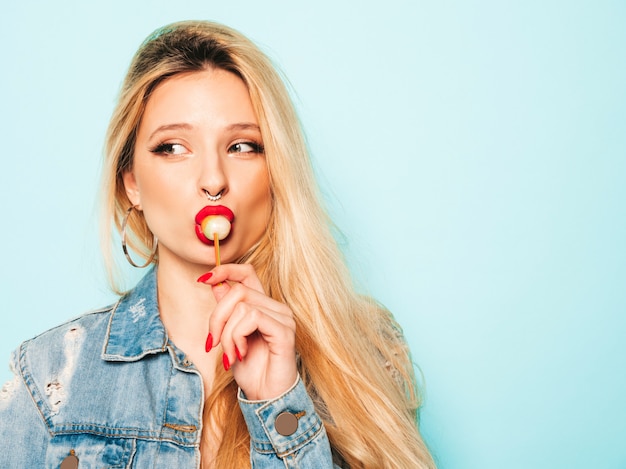 Portrait of young beautiful hipster bad girl in trendy jeans  clothes and earring in her nose.  Positive model licking round sugar candy