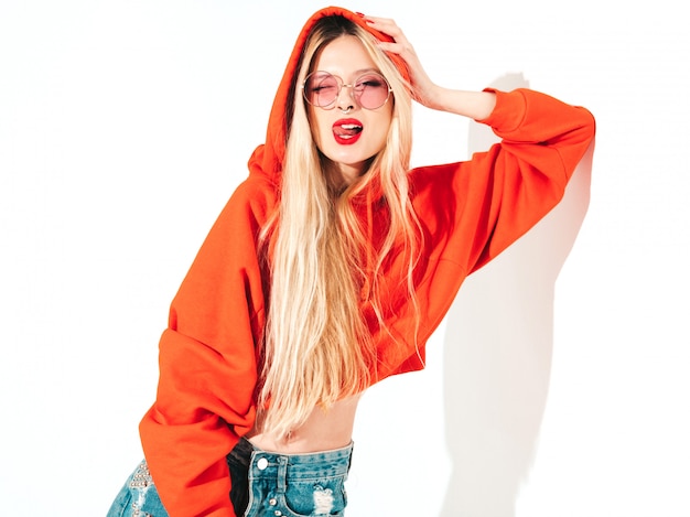 Free photo portrait of young beautiful hipster bad girl in trendy red  hoodie and earring in her nose.  positive model having fun.shows tongue