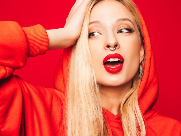 Free photo portrait of young beautiful hipster bad girl in trendy red  hoodie and earring in her nose.  positive model having fun