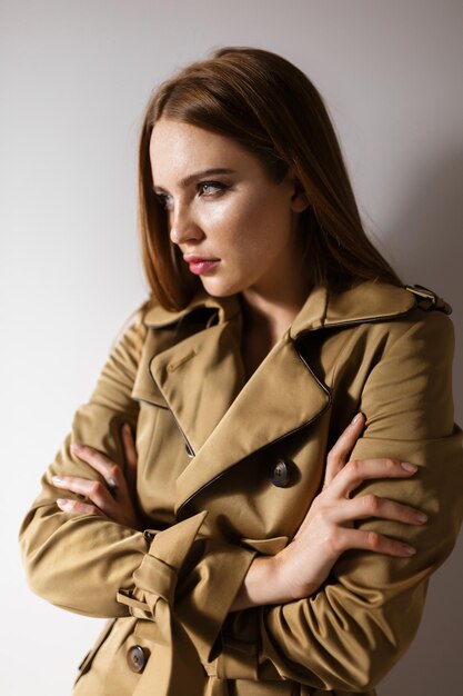 Portrait of young beautiful lady in trench coat standing and thoughtfully looking aside