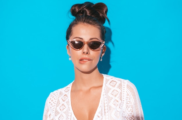 Portrait of young beautiful sexy smiling woman with ghoul hairstyle. Trendy girl in casual summer white hipster suit clothes in sunglasses. Hot model isolated on blue.Biting her lip