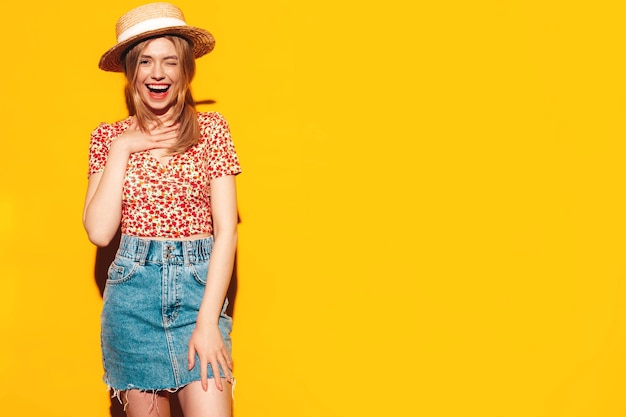 Free photo portrait of young beautiful smiling blond female in trendy summer clothes carefree woman posing near yellow wall in studio positive model having fun indoors cheerful and happy in hat