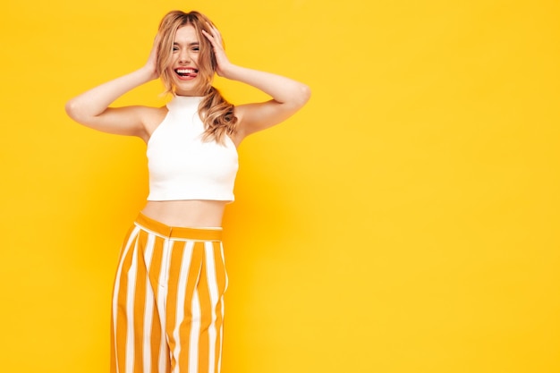 Portrait of young beautiful smiling blond female in trendy summer clothes carefree woman posing near yellow wall in studio Positive model having fun indoors Cheerful and happy