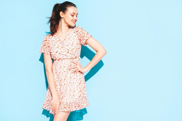 Portrait of young beautiful smiling female in trendy summer blue dress Sexy carefree woman posing near blue wall in studio Positive model having fun and going crazy Cheerful and happy