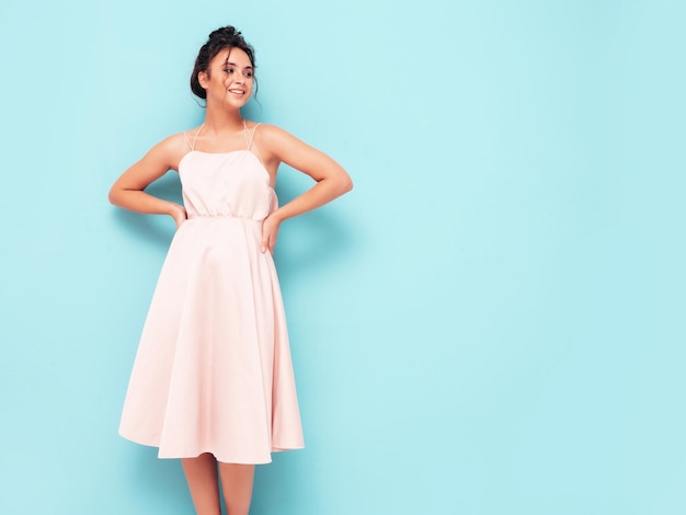 Portrait of young beautiful smiling female in trendy summer dress Sexy carefree woman posing near blue wall in studio Positive model having fun indoors Cheerful and happy