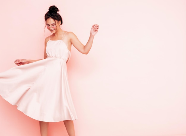 Portrait of young beautiful smiling female in trendy summer dress Sexy carefree woman posing near pink wall in studio Positive model having fun indoors Cheerful and happy