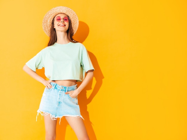 Free Photo portrait of young beautiful smiling female in trendy summer jeans skirt carefree woman posing near yellow wall in studio positive model having fun indoors cheerful and happy in hat