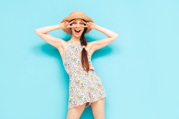 Free photo portrait of young beautiful smiling female in trendy summer overalls carefree woman posing near blue wall in studio positive model having fun indoors cheerful and happy in hat