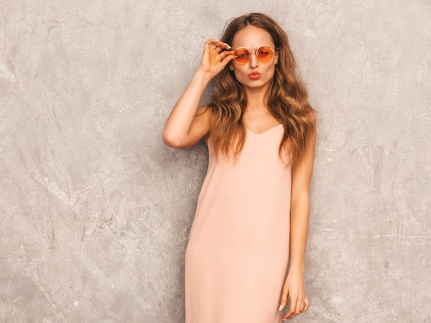 Free photo portrait of young beautiful smiling girl in trendy summer light pink dress. sexy carefree woman posing. positive model having fun in round sunglasses