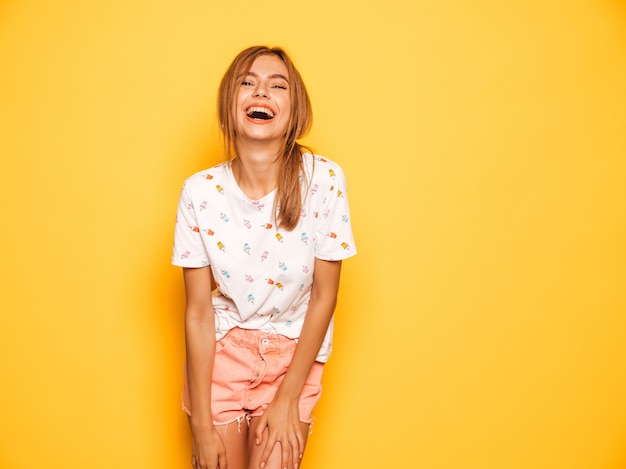 Free Photo portrait of young beautiful smiling hipster girl in trendy summer jeans shorts clothes. sexy carefree woman posing near yellow wall. positive model having fun