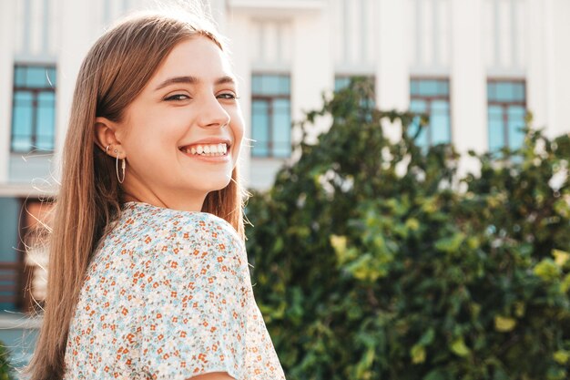 Portrait of young beautiful smiling hipster woman in trendy summer dress Sexy carefree woman posing on the street background at sunset Positive model outdoors Cheerful and happy