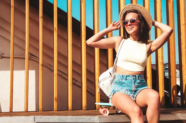 Free photo portrait of young beautiful smiling hipster woman in trendy summer jeans shorts and hat sexy carefree model posing on the street background at sunset positive model outdoors with briefcase