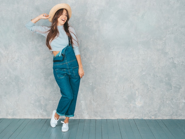 Free Photo portrait of young beautiful smiling woman looking . trendy girl in casual summer overalls clothes and hat.  