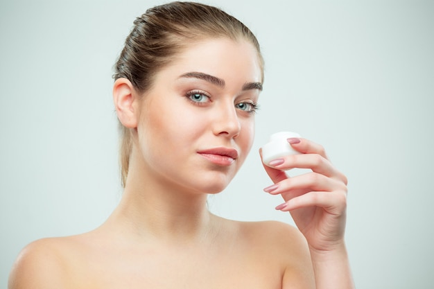 Portrait of young beautiful woman applying moisturizing cream on her face