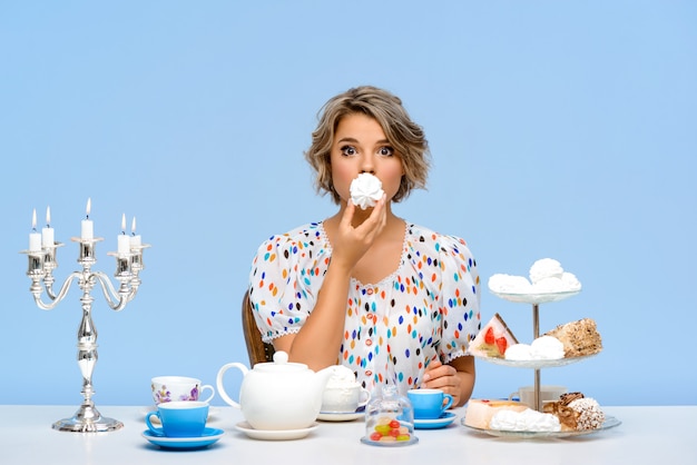 Portrait of young beautiful woman with sweets over blue wall