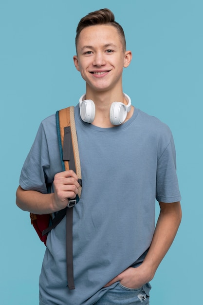 Free photo portrait of a young boy holding his backpack and his headphones