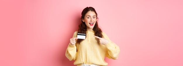 Free photo portrait of young brunette caucasian girl pointing finger at plastic credit card recommending bank g