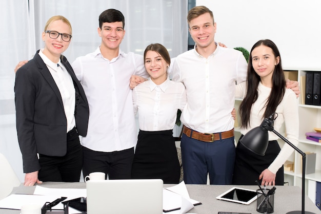 Free photo portrait of young business people with their arms around each other shoulders in the office