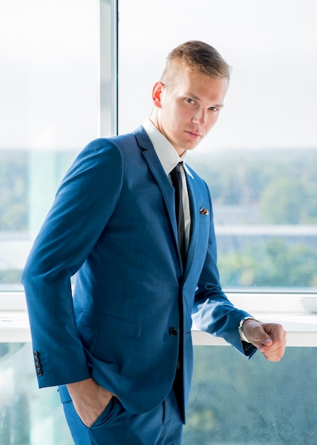 Portrait of young businessman standing near the window with hand in pocket