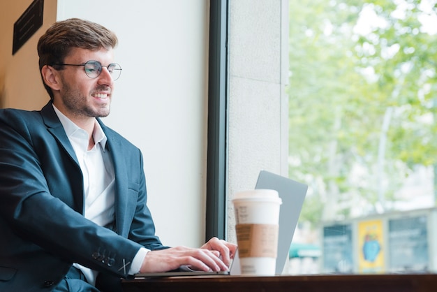 Free photo portrait of a young businessman using laptop with coffee cup on table in cafe