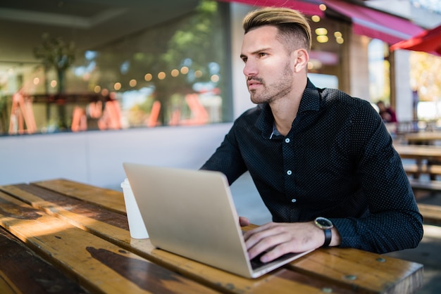 Portrait of young businessman working on his laptop while sitting in a coffee shop. Technology and business concept.