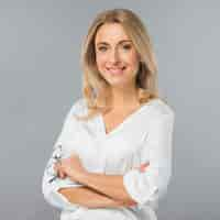 Free photo portrait of a young businesswoman holding eyeglasses in hand against gray backdrop