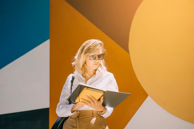 Portrait of a young businesswoman reading book standing against wallpaper