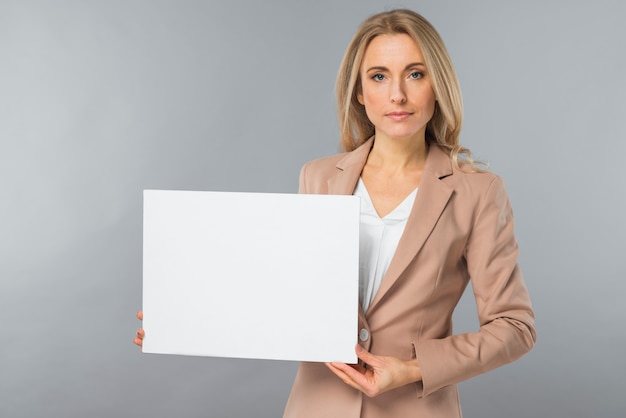 Free photo portrait of young businesswoman showing blank white placard against gray background