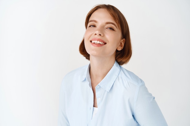 Portrait of young businesswoman smiling on white wall. Female entrepreneur in office blouse, standing motivated and self-assured