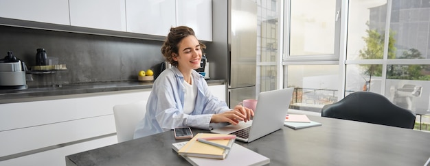 Free photo portrait of young businesswoman works from home looks at laptop and smiles