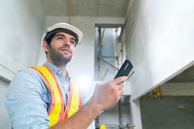 Free Photo portrait of young caucasian male engineer wearing uniform and hard hat hand use smartphont communication in site construction background