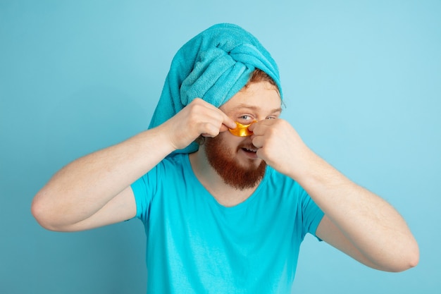 Free photo portrait of young caucasian man in his beauty day and skin care routine. male model with natural red hair applying under-eye golden patches.