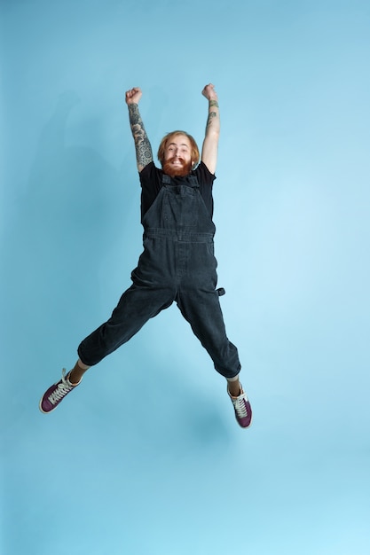 Free Photo portrait of young caucasian man looks dreamful, cute and happy. jumping. laughting on blue studio background. copyspace for your advertising. concept of future, target, dreams, visualisation.