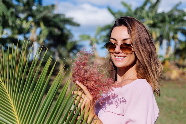 Portrait of young caucasian tanned woman in romantic pink dress round earings silver bracelet and sunglasses with wild flowers