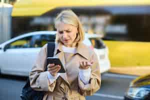 Free photo portrait of young confused blonde woman standing on busy street with cars behind her looking at