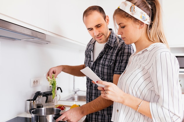 Free photo portrait of young couple reading recipe book while cooking together at the kitchen