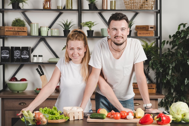 Portrait of young couple standing behind the kitchen counter with many vegetables