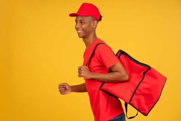 Portrait of young delivery man dressed in a red uniform running over isolated background. Delivery concept.