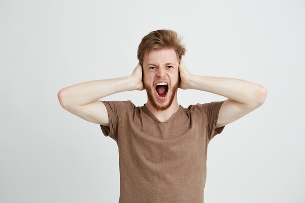 Free photo portrait of young emotive angry man closing ears shouting screaming.