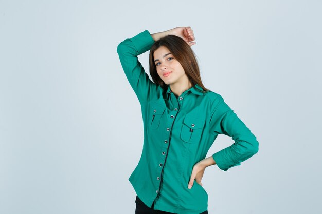 Portrait of young female holding hand on head in green shirt and looking cheerful front view