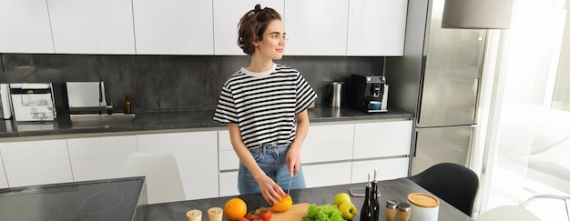 Free photo portrait of young female model cooking in the kitchen chopping vegetables vegan girl preparing meal