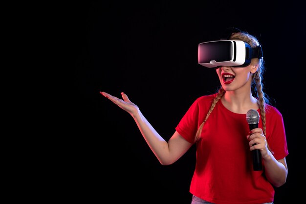 Portrait of young female playing vr and singing with mic on dark wall