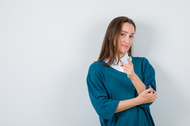 Portrait of young female pointing forward in sweater over shirt and looking sensible front view