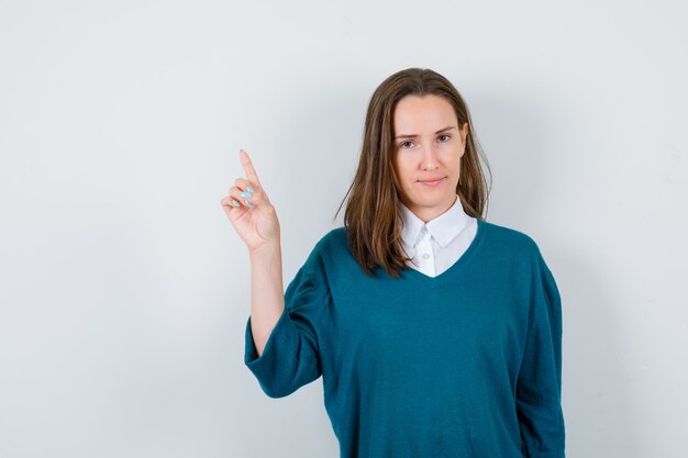 Portrait of young female pointing up in sweater over shirt and looking confident front view