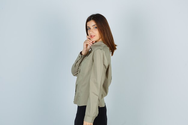 Portrait of young female posing while holding her chin with hand in shirt, skirt and looking confident