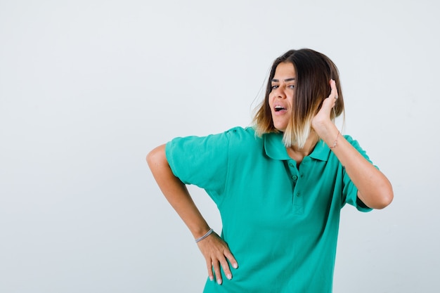 Portrait of young female posing while keeping hand on head in polo t-shirt and looking glad front view